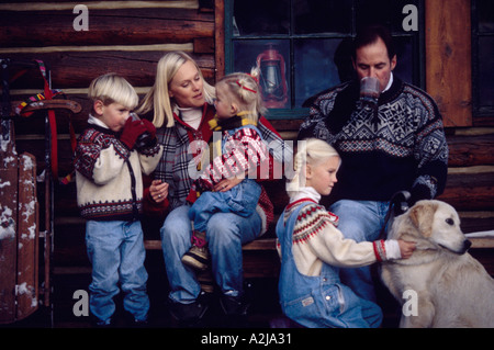 Un couple et trois enfants ensemble à l'extérieur d'une cabane sur un jour froid de boire des boissons chaudes et de jouer avec leur chien Banque D'Images