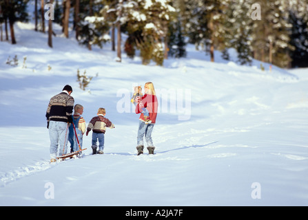 Un père tire un traîneau comme il suit sa femme et leurs trois enfants dans un champ neigeux Banque D'Images