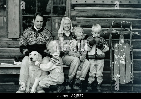 Un couple et trois enfants ensemble à l'extérieur d'une cabane sur un jour froid de boire des boissons chaudes et de jouer avec leur chien Banque D'Images