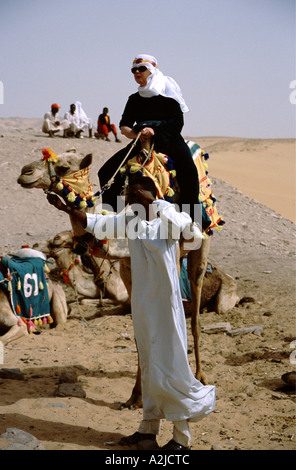 Afrique - Egypte - Aswan - Nubian chamelier mène à touristiques foulard sur l'ensemble de chameau desert Banque D'Images