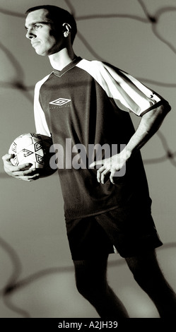 Une couleur/noir et blanc photographie d'un homme blanc portant de 20 à 25 ans et kit de football jouer au football/soccer dans un studio. Banque D'Images