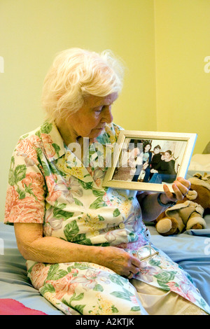 Geriatric/vieille femme assis sur le bord du lit dans la maison de soins infirmiers à la photo de famille à Banque D'Images