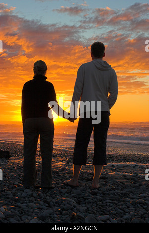 Jeune couple tenir la main alors que le soleil se couche sur la mer de Tasman à Greymouth sur l'île du Sud, Nouvelle-Zélande. Banque D'Images