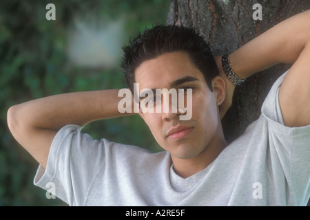 La moitié de 22 ans caucasien homme moitié mexicaine avec 'hands behind head' leaning against tree Banque D'Images