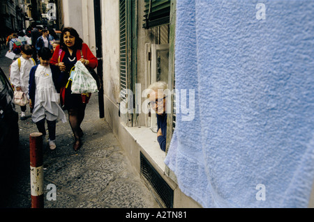 Vieille Femme sortir de la fenêtre à regarder la femme comme elle marche passé qui tient la main de scène de rue fille naples Banque D'Images