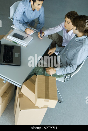 Trois collègues hommes regroupés autour de 24, entouré par des boîtes de carton Banque D'Images