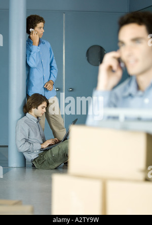 Les collègues de sexe masculin à l'aide d'ordinateur portable et téléphone cellulaire, les boîtes en carton en premier plan Banque D'Images