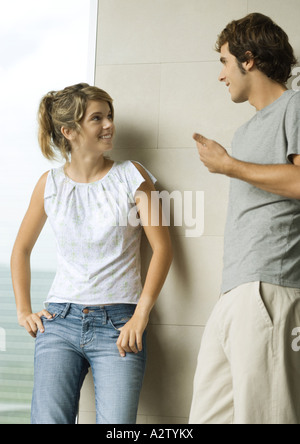 Young man and woman leaning against wall, talking and smiling Banque D'Images