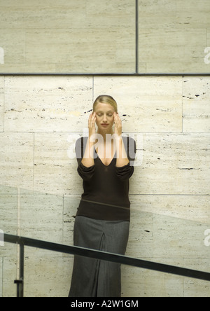 Woman leaning against wall, holding head, les yeux fermés Banque D'Images