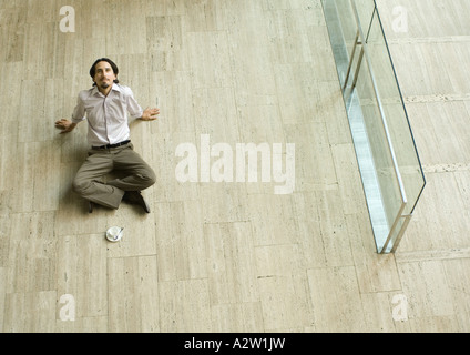 Homme assis sur le plancher avec une tasse à café en face de lui, se penchant en arrière, high angle view Banque D'Images