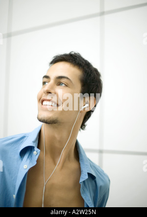 Young man listening to earphones, smiling Banque D'Images