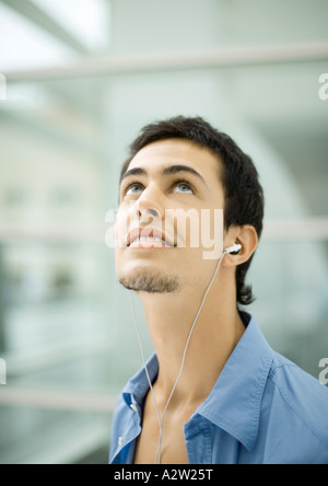 Young man listening to earphones, looking up Banque D'Images