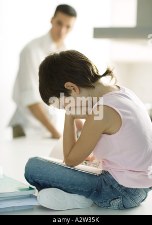 Enfant assis sur le comptoir à faire leurs devoirs tout en père repas cuisiniers Banque D'Images