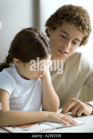 Adolescent à l'écoute de petite soeur lire Banque D'Images