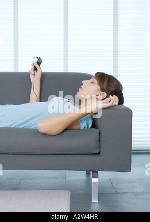 Young woman lying on sofa, à l'écoute de lecteurs MP3 player Banque D'Images