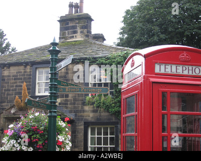 Boîte de téléphone rouge avec panneaux verts à Bronte Parsonage avec Yorkshire typique pub derrière, Haworth, West Yorkshire, England, UK Banque D'Images