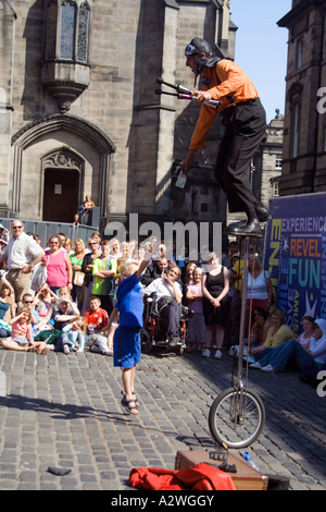 Petit garçon sautant vers le haut pour un billet détenu par un artiste de rue sur un monocycle, Edinburgh Festival Fringe, en Écosse. Banque D'Images