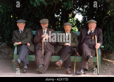 Quatre vieux hommes portant des chapeaux en tissu. Assis sur le banc de parc. Banque D'Images