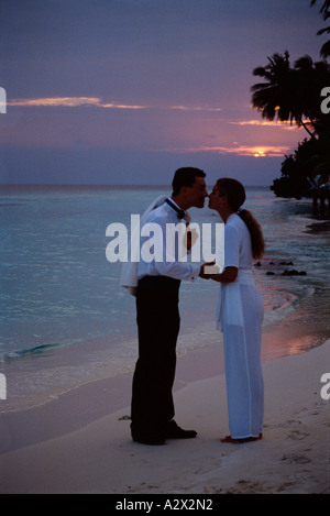Les Maldives. Jeune couple dans le soir vêtements standing on tropical beach au coucher du soleil. Banque D'Images