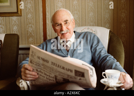 Old English homme assis dans un fauteuil. Avec Sunday Telegraph Journal et tasse de thé. Banque D'Images