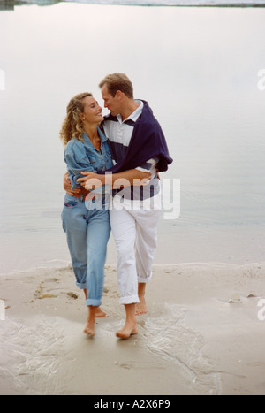 Jeune couple marchant pieds nus sur la plage. Banque D'Images