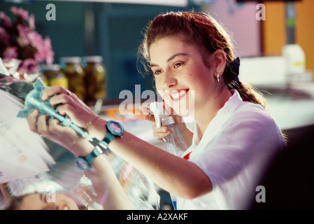 Jeune femme travaillant à l'intérieur dans les locaux de l'alimentation au détail, nettoyage vitre vitrine. Banque D'Images