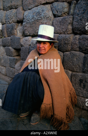 Une femme autochtone portant un chapeau appuyé contre un vieux mur de pierre Inca à Cusco. (Cuzco). Banque D'Images