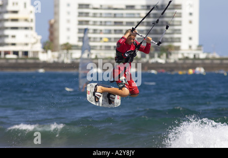 Jeune homme kitesurfer en rouge saute haut une vague sur sa planche en face des hôtels et appartements de plage El Medano Banque D'Images