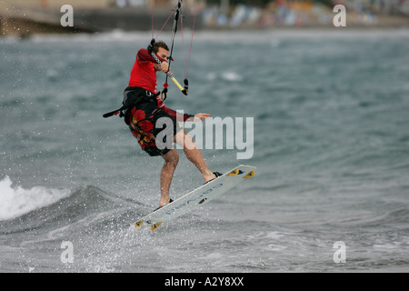 Homme kitesurfer en rouge ascenseurs sa planche à l'extérieur de l'eau au large de la plage de El Medano Tenerife Espagne Banque D'Images