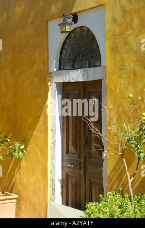 Kastellorizo porte avec fenêtre en arc au-dessus et installé dans un mur jaune. Il y a une lampe au-dessus de la porte et des pots de plantes soit Banque D'Images