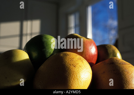 Les oranges et les pommes dans un bol de fruits avec le coucher du soleil la lumière sur eux et un ciel bleu à travers une fenêtre montrant en arrière-plan Banque D'Images