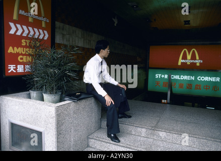 Un homme d'affaires en costume et cravate, avec des lunettes et un porte-documents se trouve à l'entrée d'un McDonalds à Bangkok, Thaïlande Banque D'Images