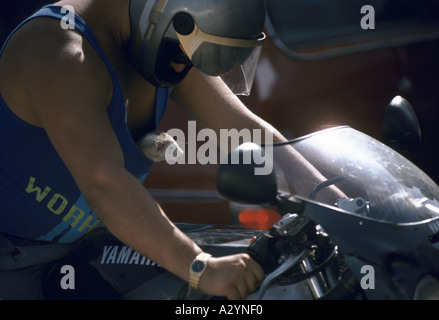 Un homme sur une moto Yamaha regarde affectueusement de son casque à l'open mouthed ferret poussant hors de son débardeur bleu Banque D'Images