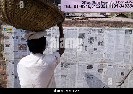 Un homme de prendre une minute pour lire le journal qui est publié quotidiennement sur un mur à l'extérieur pour l'usage public à Dhaka Bangladesh Banque D'Images