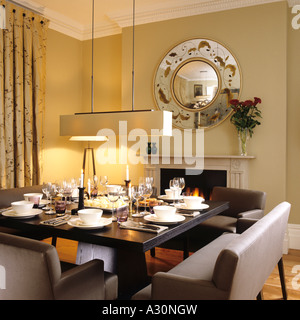Square table de salle à manger avec banquette double coin et feu ouvert sous miroir circulaire Banque D'Images