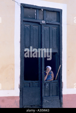 Jeune femme portant un foulard de Cuba, à la recherche à partir d'une fenêtre ouverte dans une vieille porte en bois à Trinidad, Cuba Banque D'Images