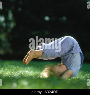 Petite fille allongé dans l'herbe sur son dos avec ses jambes en l'air et sur son corps s'étend son dos Banque D'Images