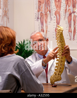 Un chiropraticien brandissant une modèle de la colonne vertébrale humaine tout en parlant à un patient Banque D'Images