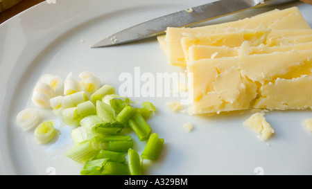 Ferme à maturité le cheddar et oignons de printemps en morceaux sur une plaque avec un couteau Banque D'Images