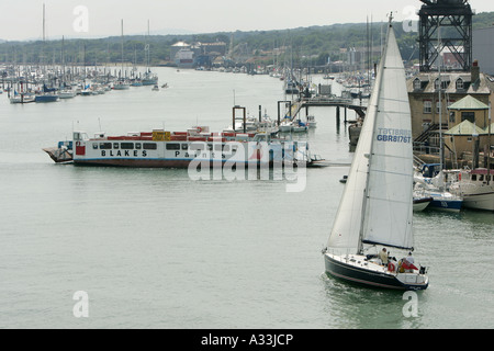 Ferry de la chaîne prend de passagers sur le port de Cowes sur l'île de Wight comme un yacht passe l'entrée du port Banque D'Images