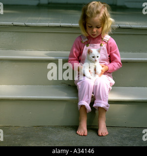 Girl wearing pink et combinaisons blanches assis sur sa terrasse de marches pour la tenue d'un peu de blanc chaton dans ses bras Banque D'Images