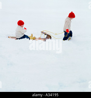 Un jeune enfant sur un autre enfant tirant un traîneau type luge dans la neige Banque D'Images