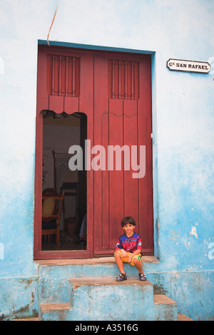 Jeune garçon assis sur une porte en face d'une maison, Camaguey, Cuba, Camagüey Province Banque D'Images