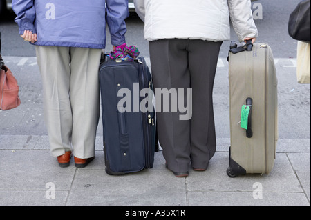 Moitié inférieure de deux femmes âgées debout avec des valises sur le trottoir par le côté d'une route en attente sur un taxi à Dublin Banque D'Images