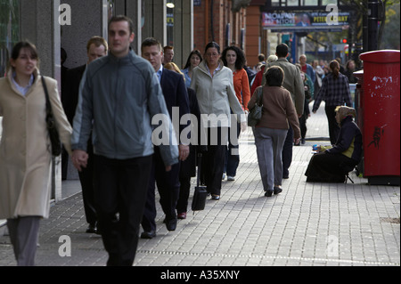 Les piétons circulant de l'Europe de l'est passé à la gitane mendiant femme assise sur le trottoir à côté de red post box à Belfast Banque D'Images