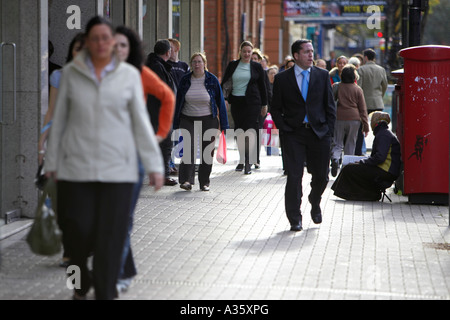 Les piétons circulant de l'Europe de l'est passé à la gitane mendiant femme assise sur le trottoir à côté de red post box à Belfast Banque D'Images