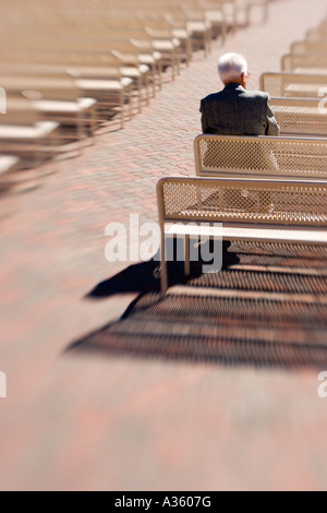 Un vieil homme solitaire assise seule dans les rangées de bancs vides. Banque D'Images