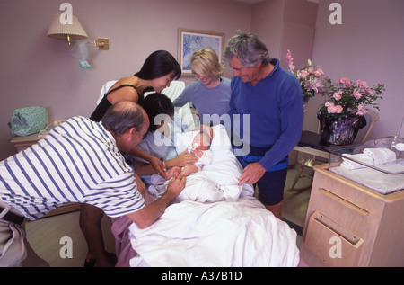 Fier père et amis venus rendre visite à femme avec bébé nouveau-né à l'hôpital salle de réveil Banque D'Images
