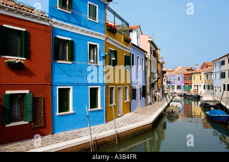 Italie Vénétie Lagune de Venise Burano Island maisons colorées à côté de canal avec les touristes en passant devant des bateaux amarrés le long de canal Banque D'Images