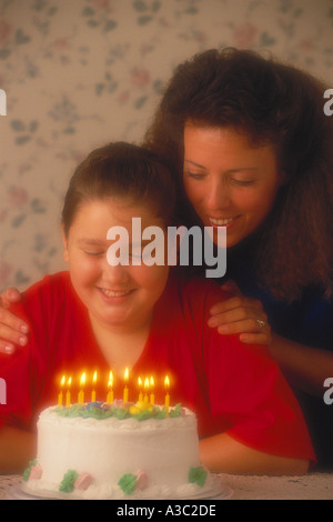 Une jeune fille qui célèbre son 12ème anniversaire par la préparation de souffler les bougies sur son gâteau comme maman observe Banque D'Images